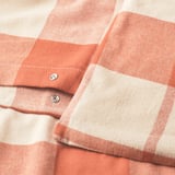 Primeiro plano de tecido de flanela vermello-marrón con detalle de peche de sobr.