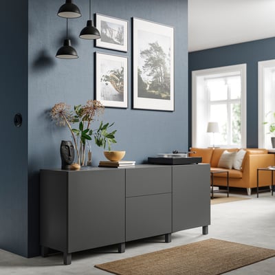 Sala de estar moderna cunha unidade de almacenamento gris BESTÅ, con lámpadas colgantes, arte enmarcada, flores secas e un sofá laranxa.