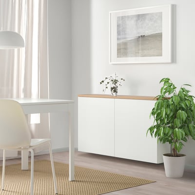 Unidade de almacenamento moderno BESTÅ con armario único, tapa de madeira, arte de praia, plantas e escritorio.