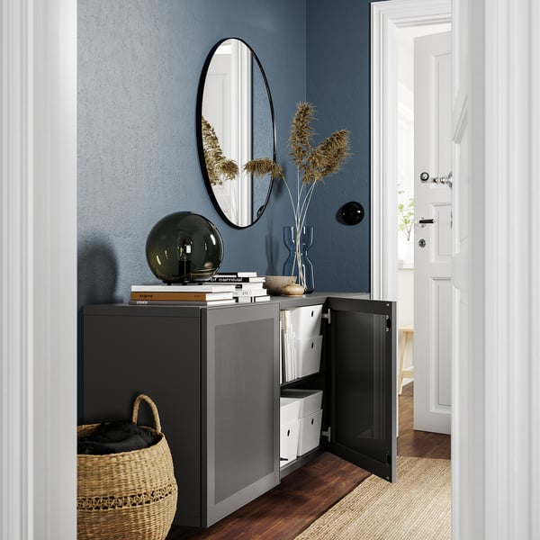 Armario gris moderno con porta aberta, espello, lámpada e vaso. Cesta de rafia, parede azul.
