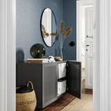 Armario gris moderno con porta aberta, espello, lámpada e vaso. Cesta de rafia, parede azul.