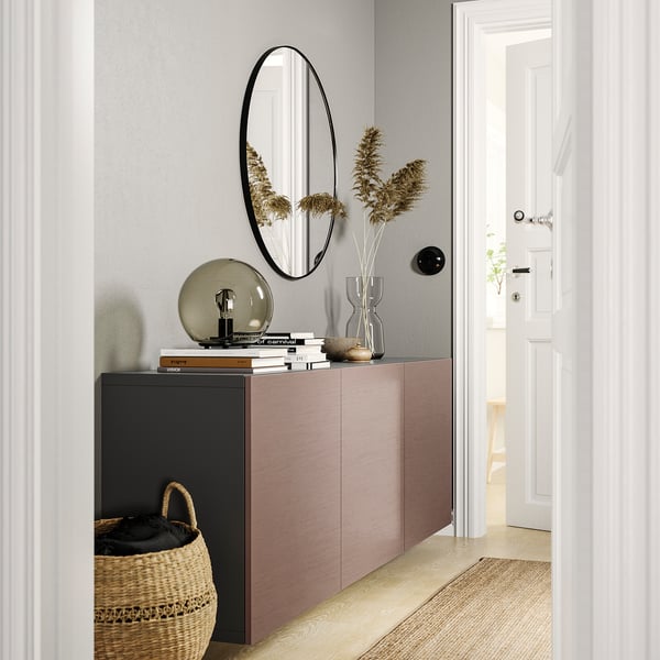 Entrada moderna e minimalista con sideboard rosa claro BESTÅ, espello redondo, lámpada, libros, vaso con flores secas e cesta de vimbio.