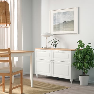 Habitación minimalista moderna con sideboard branco BESTÅ, mesa de madeira, alfombra beige e planta de casa grande.