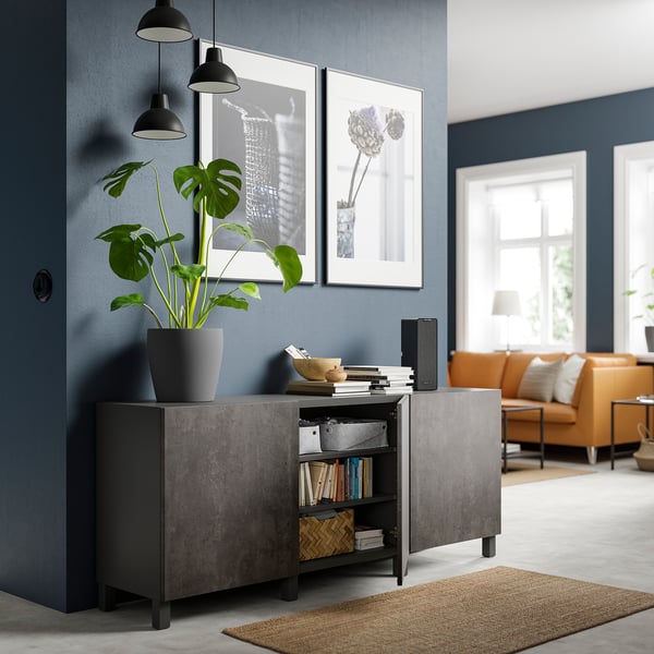 Sala de estar moderna con sideboard gris escuro BESTÅ, planta de casa, lámpadas colgantes, arte enmarcada.