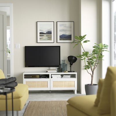 Sala de estar moderna con soporte de televisión BESTÅ, televisión montada, estampados da natureza, cadeiras amarelas, alfombra de plantas, beige.
