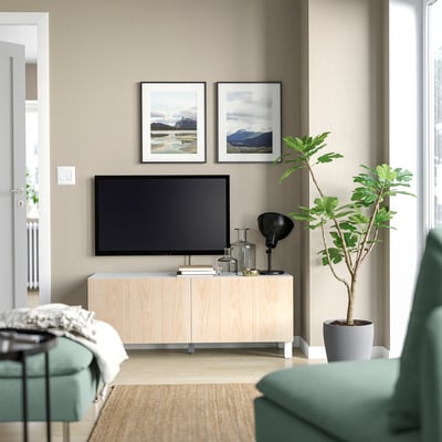 Salón minimalista moderna, un soporte de televisión de madeira de cor clara cunha pantalla plana, dúas estampas naturais, unha planta verde e unha cadeira azul.