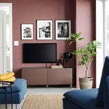Sala de estar moderna con paredes borgoña, sofá azul, televisión en consola rosada, elementos decorativos e fotos enmarcadas.