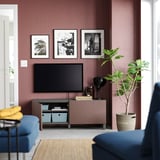 Salón moderno con paredes marróns, sofá azul, televisión, planta en pota, lámpada e imaxes enmarcadas nun banco de televisión rosa BESTÅ.