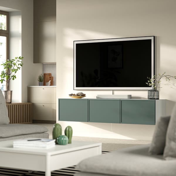 Sala de estar moderna con banco de televisión BESTÅ de prata, portas verdes, sofá gris, mesa de café branca e verde decorativo.