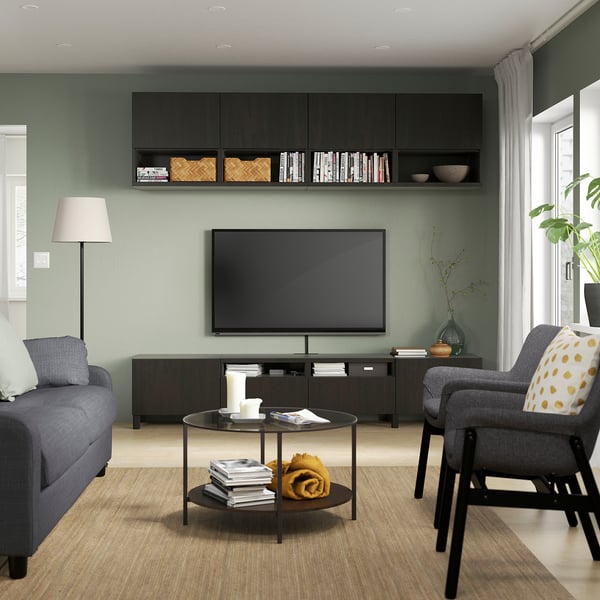 Sala de estar acolledora con televisión na unidade BESTÅ, libros, manta amarela, sofá gris, paredes verdes e lámpada.