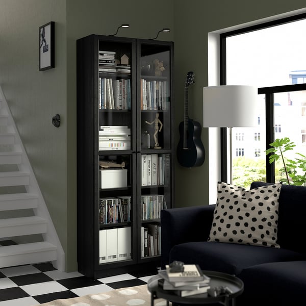 Libraría BILLY negra con libros e decoración por escaleiras brancas. Sofá escuro, guitarra, xanela de vista á cidade.