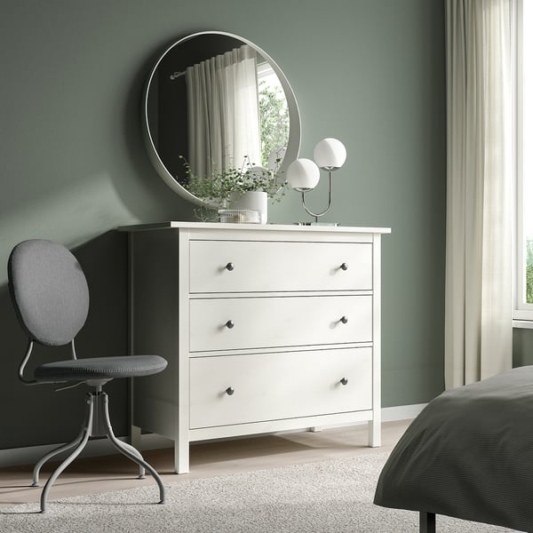 Dormitorio minimalista con cadeira BJÖRKBERGET, mesa, espello e lámpadas. Caixóns brancos, roupa de cama a raias, parede verde.