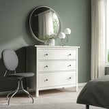 Dormitorio minimalista con cadeira BJÖRKBERGET, mesa, espello e lámpadas. Caixóns brancos, roupa de cama a raias, parede verde.