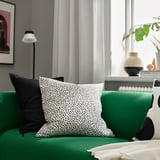Sofá verde, almofada punteada, lámpada branca, vasos - sala de estar.