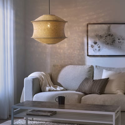 Sala de estar acolledora con cálida lámpada colgante BLÅSTÅNG sobre o sofá, arte abstracta da parede, mesa de café con libros e cunca.