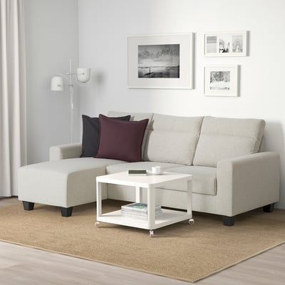 Sala de estar moderna con sofá gris en forma de L BOLLSTANÄS, alfombra natural, mesa de café branca e lámpada branca.