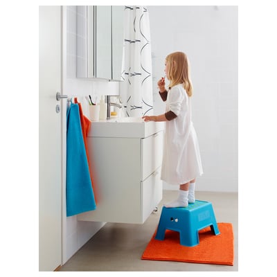 Un neno está nun taburete azul e antiesvarádante para chegar a un lavabo de baño, aprendendo a cepillar os dentes.