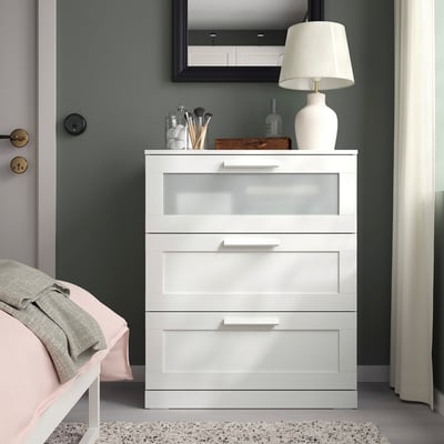 Cofre branco BRIMNES con caixón de vidro, espello, lámpada e cama no cuarto.