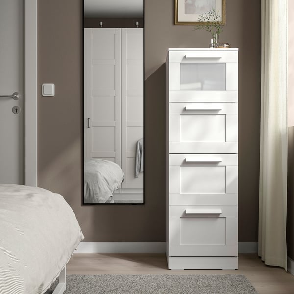 Moderno peito branco BRIMNES, deseño alto, elegante con parte superior de vidro, está xunto á cama, xunto ao armario.