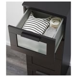 Cofre negro con caixón superior de vidro xeado, que sostén camisa e xersei raiados, caixóns de correr lisos, necesita ancoraxe na parede.