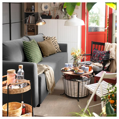 Sala de estar moderna con sofá BRISSUND gris, mesas de madeira, almofadas con patróns e decoración acolledora.