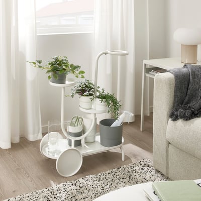 As plantas brancas multinivel están preto da luz con plantas, tesoiras e tecidos. Inclúe unha mesa pequena e un lanzamento gris.