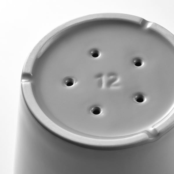 Primeiro plano en branco e negro dunha base de vasos de plantas redondas, con catro buratos de drenaxe e o número 12 en relevo.