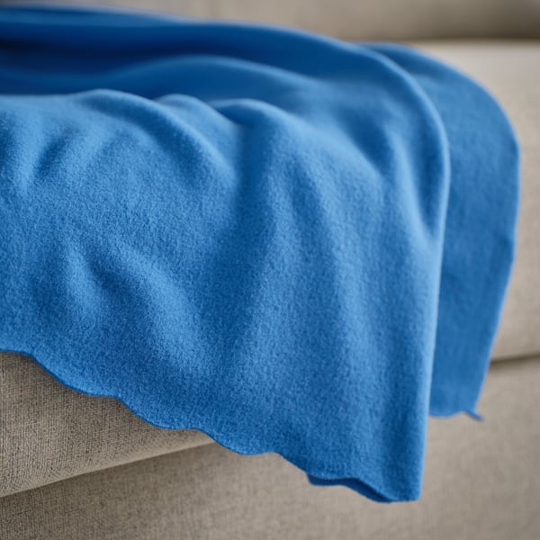 Manta de fleece azul brillante sobre un sofá beige, mostrando a súa textura suave.