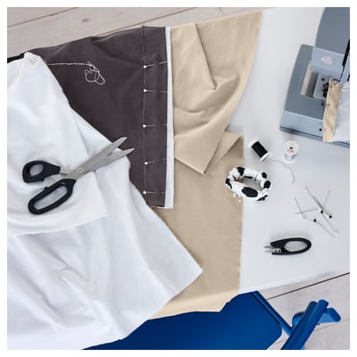Vista superior de materiais de coser: tecidos, tesoiras, fío, pins, rasador de costuras, máquina de coser sobre superficie branca.