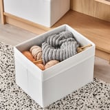Caixa de almacenamento branca na alfombra con materiais de tricotado. Sostén fíos e agullas de tricotación, encaixa nos estantes.