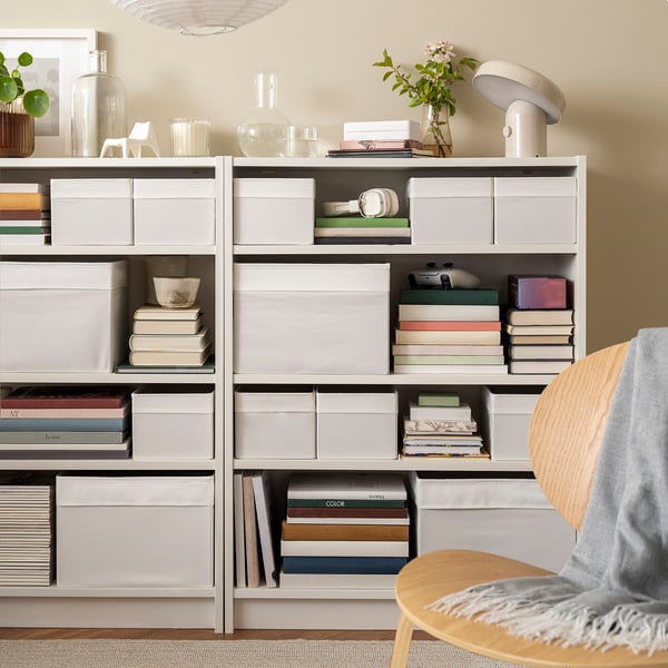 Caixas DRÖNA brancas en estantes grises, gardando libros e decoración, optimizando o espazo.