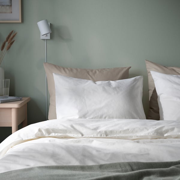 Dormitorio acolledor con roupa de cama branca DVALA. Almofadas de algodón suaves na parede verde.