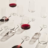 Vasos sobre a mesa, dous cheos de viño tinto, outros baleiros, todos claros e ben feitos.