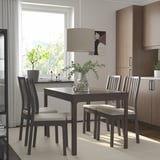 Conxunto de comedor moderno con mesa de madeira escura e cadeiras beige. Grandes fientrenas, arte, plantas.