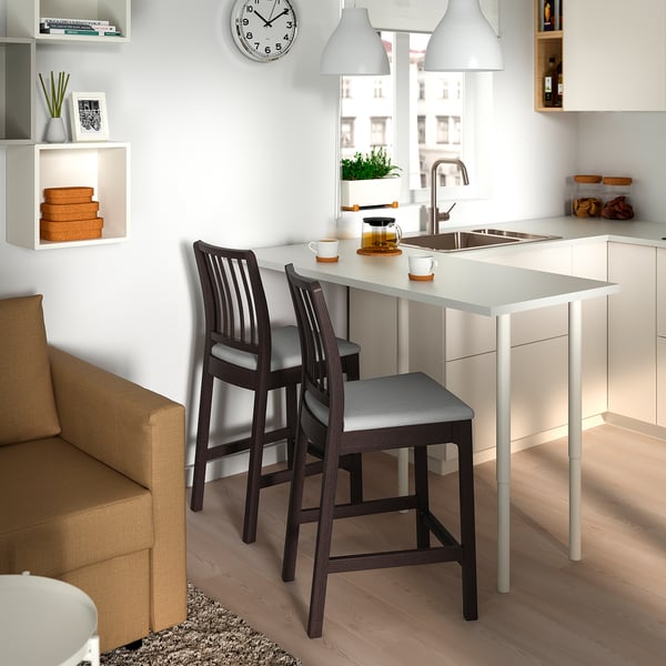 Cociña moderna con mostrador e taburetes brancos EKEDALEN, lámpadas colgantes, sofá beige, estante.