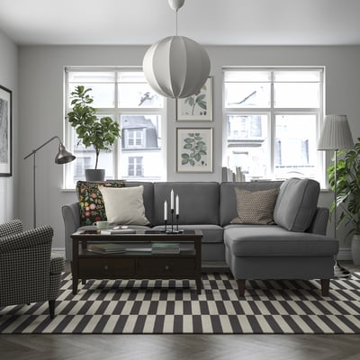 Sofá seccional gris EKHOLMA con liñas limpas, coxíns, luz natural, plantas e almofadas de cores.