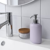 Dispensador de xabón de lavanda preto do lavabo, con billa de cromo e frasco de vidro que sostén roldas de algodón sobre a mesa branca.