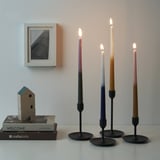 Catro velas acesas con vimbios de cores nunha mesa, xunto a libros e unha casa de paxaros, cunha imaxe enriba.