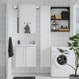 Baño moderno con vaidade branca ENHET, estantes de almacenamento abertos e lavadora. O espello e as plantas engaden estilo.