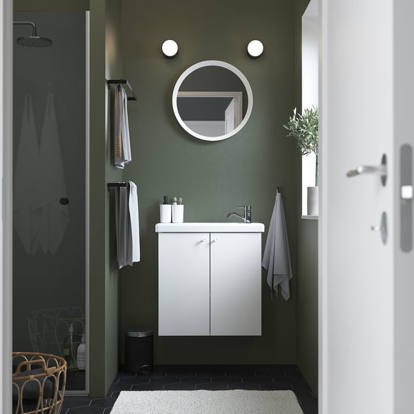 Baño verde moderno con vaidade ENHET branca, espello redondo, luces de parede, toallas grises e unha porta de ducha de cristal.