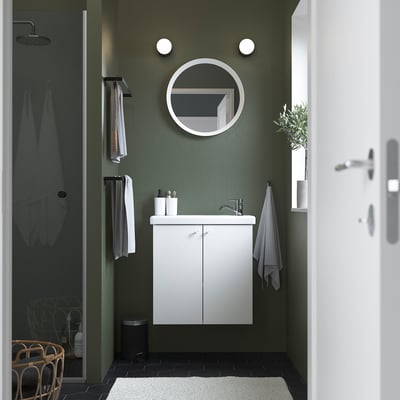 Baño verde moderno con vaidade ENHET branca, espello redondo, luces de parede, toallas grises e unha porta de ducha de cristal.