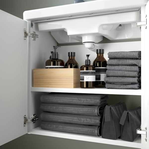 Armario de baño aberto que mostra toallas, produtos de baño e caixa de madeira nos estantes.