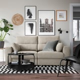 Sala de estar moderna con sofá beige, almofadas, mesa de café negra e arte de parede. Espazo e relaxante.