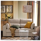 Sala de estar acolledora con sofá ESKILSTUNA beige, almofada de mostaza, lámpada tecida e mesa lateral con cunca.