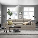 Un salón moderno con sofá ESKILSTUNA, mesa de café, alfombra, luz colgante e fiestras.