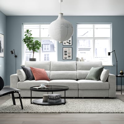 Sala de estar moderna con sofá ESKILSTUNA gris, parede azul, mesa de café redonda, luz colgante e decoración acolledora.