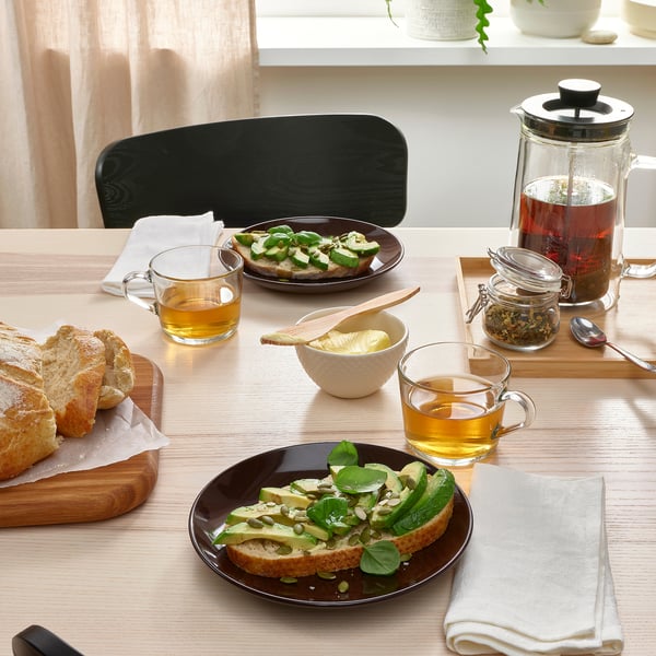 Mesa de cociña con pratos laterais FÄRGKLAR cheos de tostadas de aguacate, pan, cuncas de té e unha teteira.
