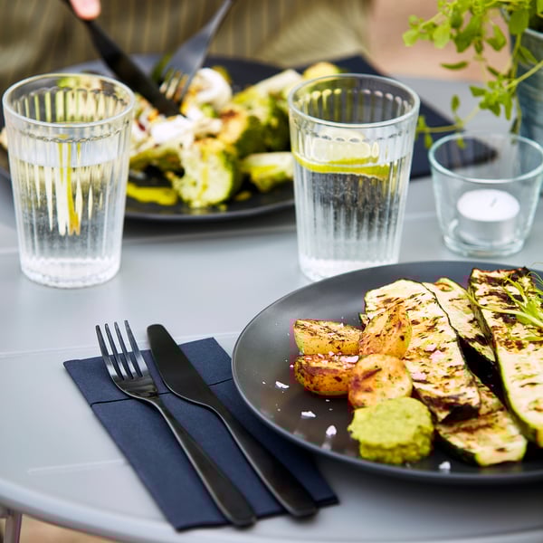 Mesa con vaixelas FÄRGKLAR: pratos, vasos, cubertas e verduras á prancha.