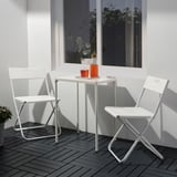 Pequena mesa e cadeiras de metal branco ao aire libre con cuncas laranxas, perfectas para balcóns.