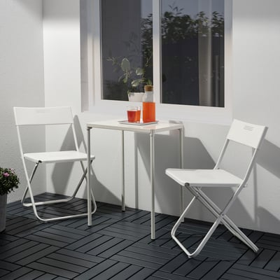 Pequena mesa e cadeiras de metal branco ao aire libre con cuncas laranxas, perfectas para balcóns.